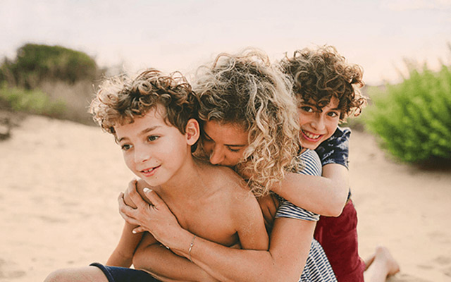 Mulher a abraçar duas crianças na praia  
