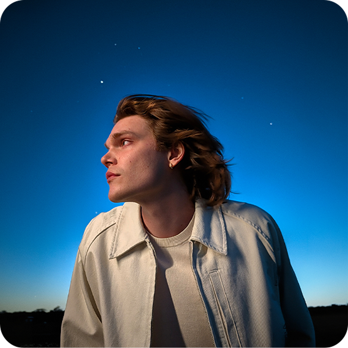 Imagem de um homem com um casaco branco no exterior, em condições de pouca luz. 